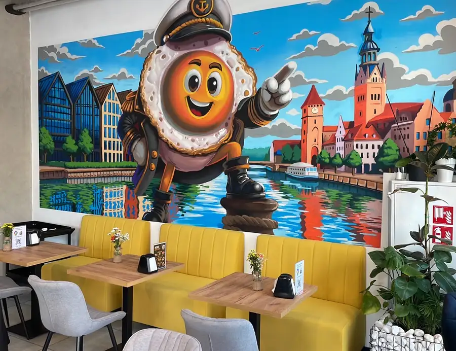 Mural z jajkiem w czapce kapitana na tle Elbląga i musztardowe kanapy